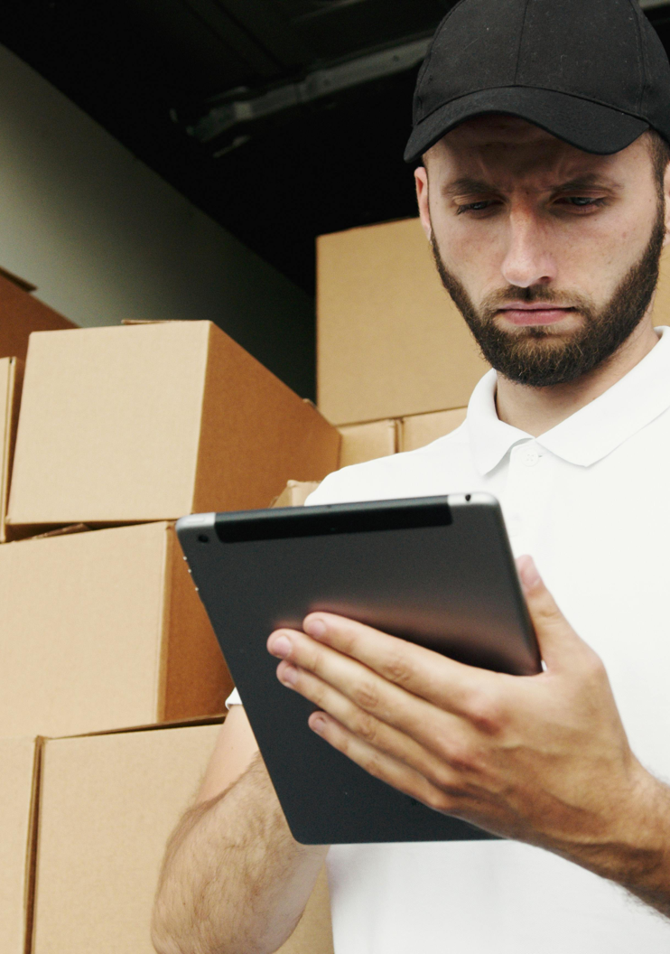 Delivery worker using a tablet to manage shipments with stacked boxes in the background.